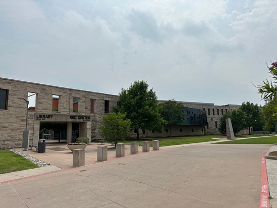 Exterior view of the Wylie Library and Recreation Center showing the modern stone façade, spacious sidewalk, trees, landscaping, and entrance clearly marked with signage.