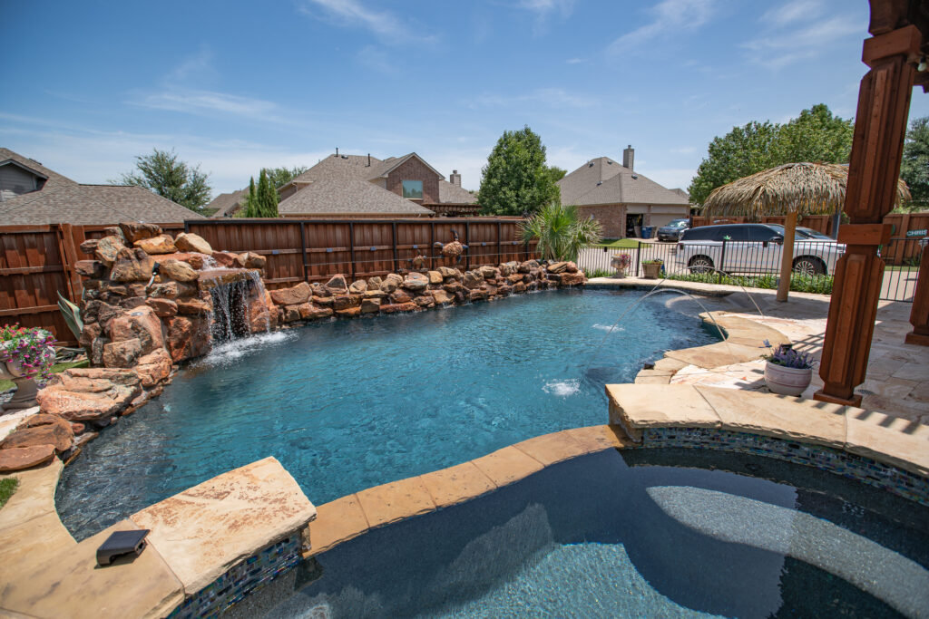 View of rock waterfall and pool jets with surrounding fence and landscaping