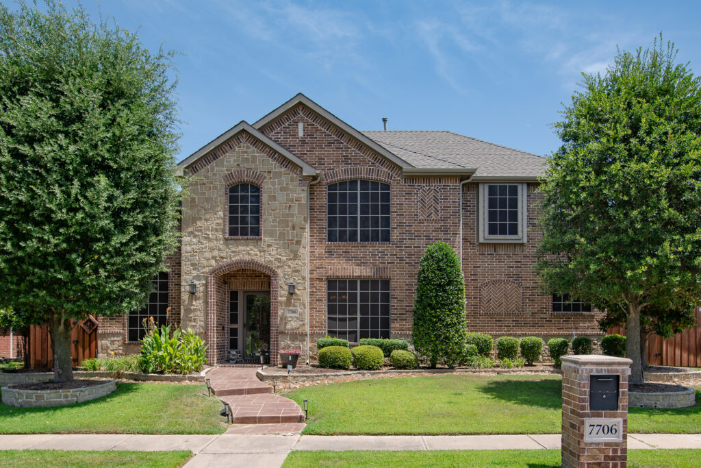 Two-story brick and stone home with manicured front lawn and walkway
