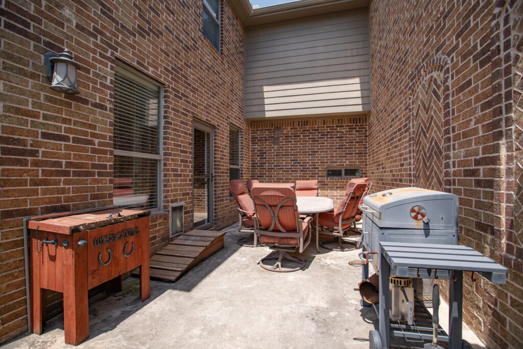 Brick courtyard with grill, round dining table, and rustic drink cooler