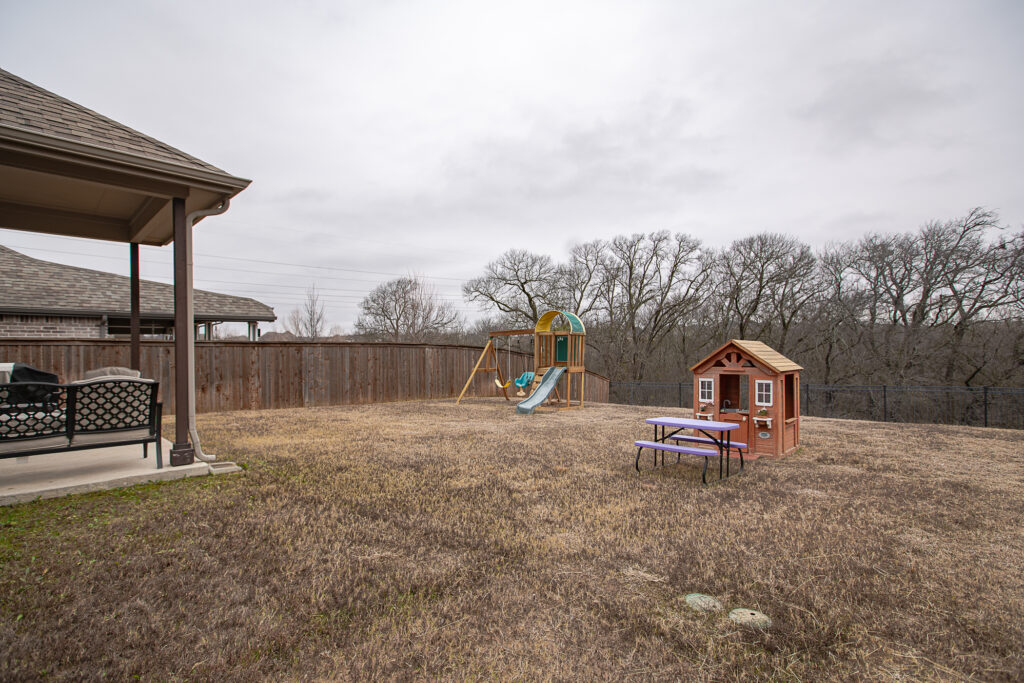 Large backyard with swingset and playhouse near wooded area