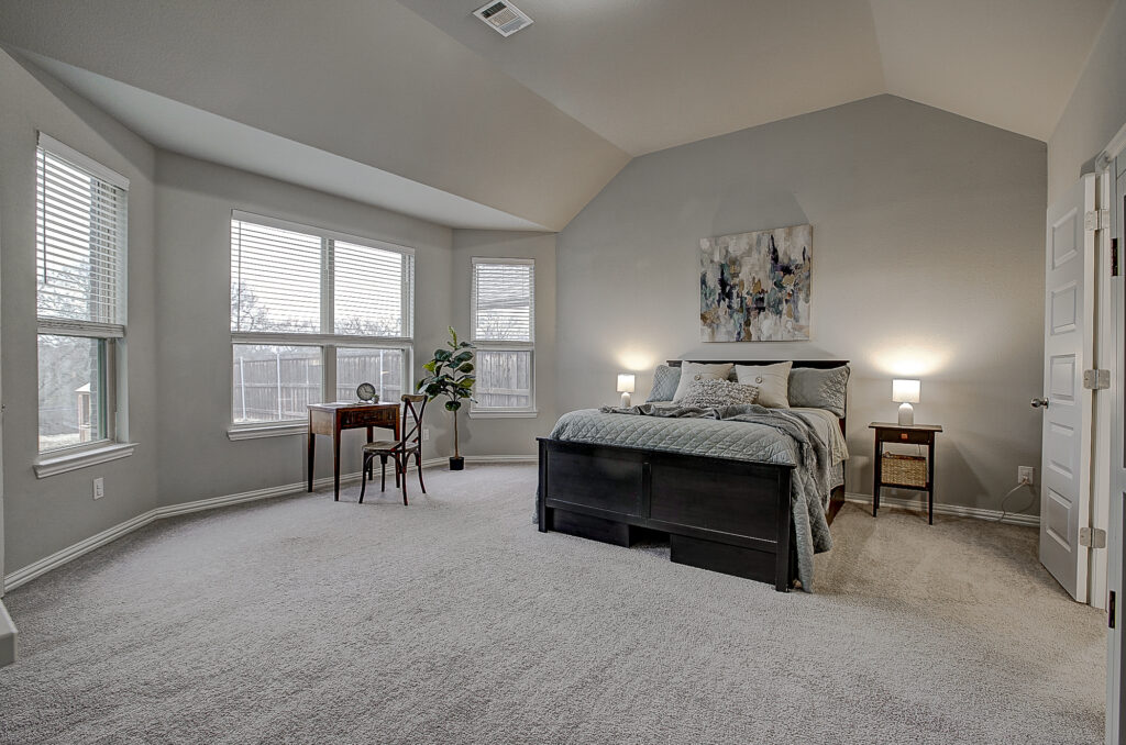 Spacious primary bedroom with vaulted ceiling and abundant natural light through large windows