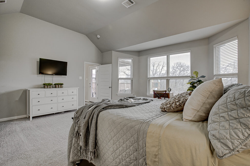Primary bedroom with side view showing TV, dresser, and nearby access to patio