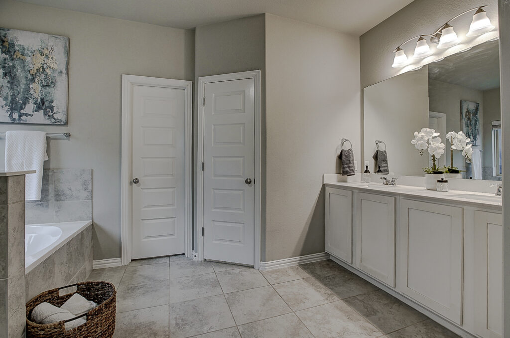 Modern primary bathroom with double sinks, wide mirror, and tile flooring