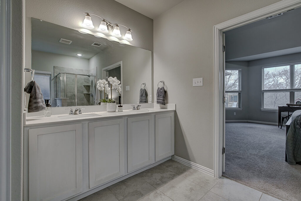 Double vanity in primary bath with modern lighting and view into the bedroom