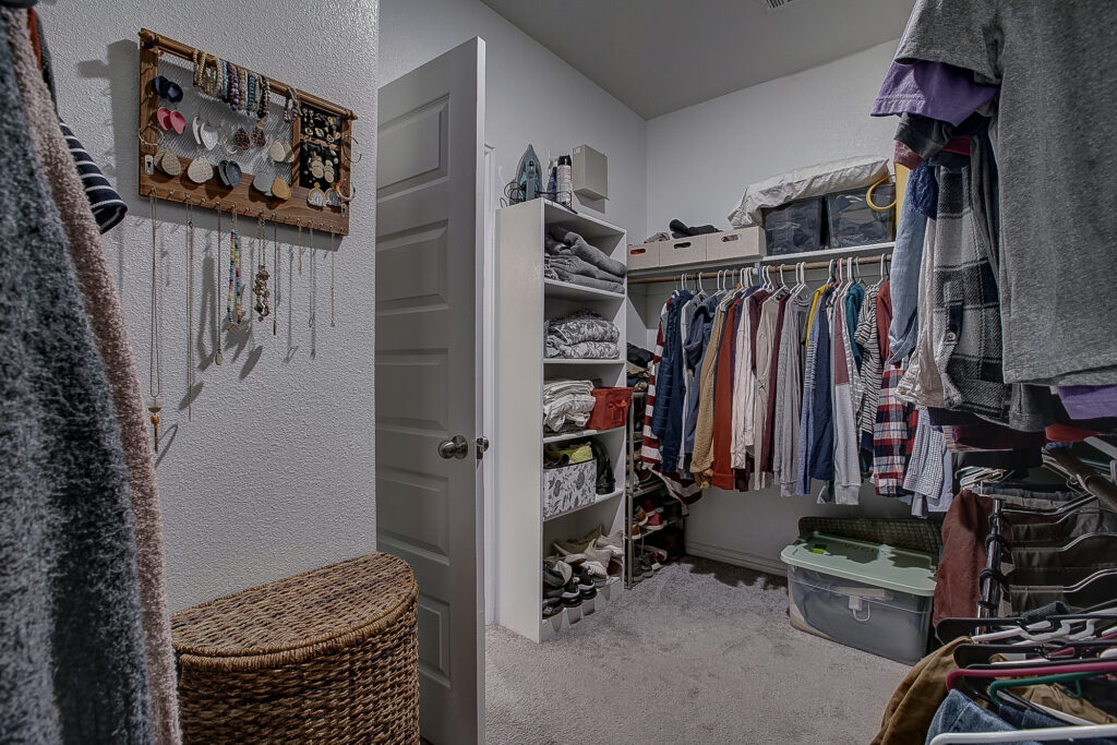 Primary closet with built-in shelving, storage bins, and organized hanging space