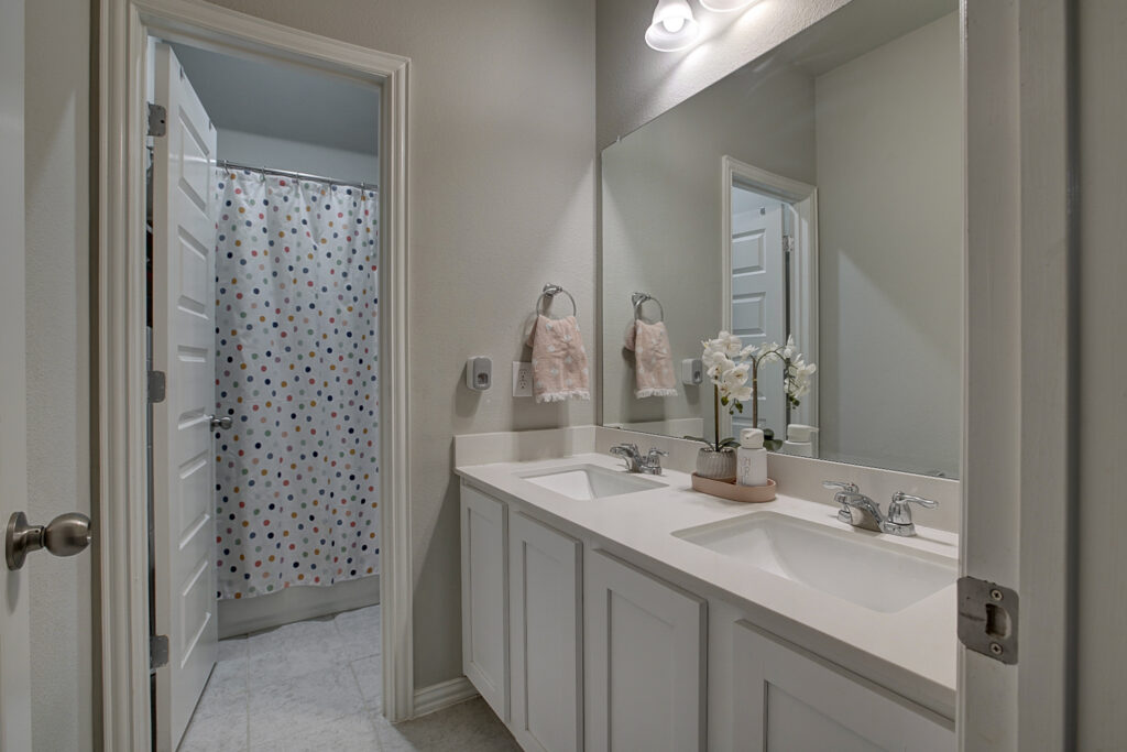 Secondary bathroom with double vanity and view into shower area with polka dot curtain