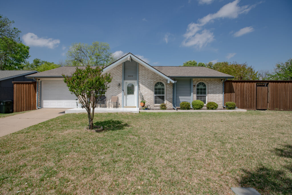 Front exterior of 5302 Saddleback Rd Garland TX with light brick façade, arched windows, covered entry, and front lawn