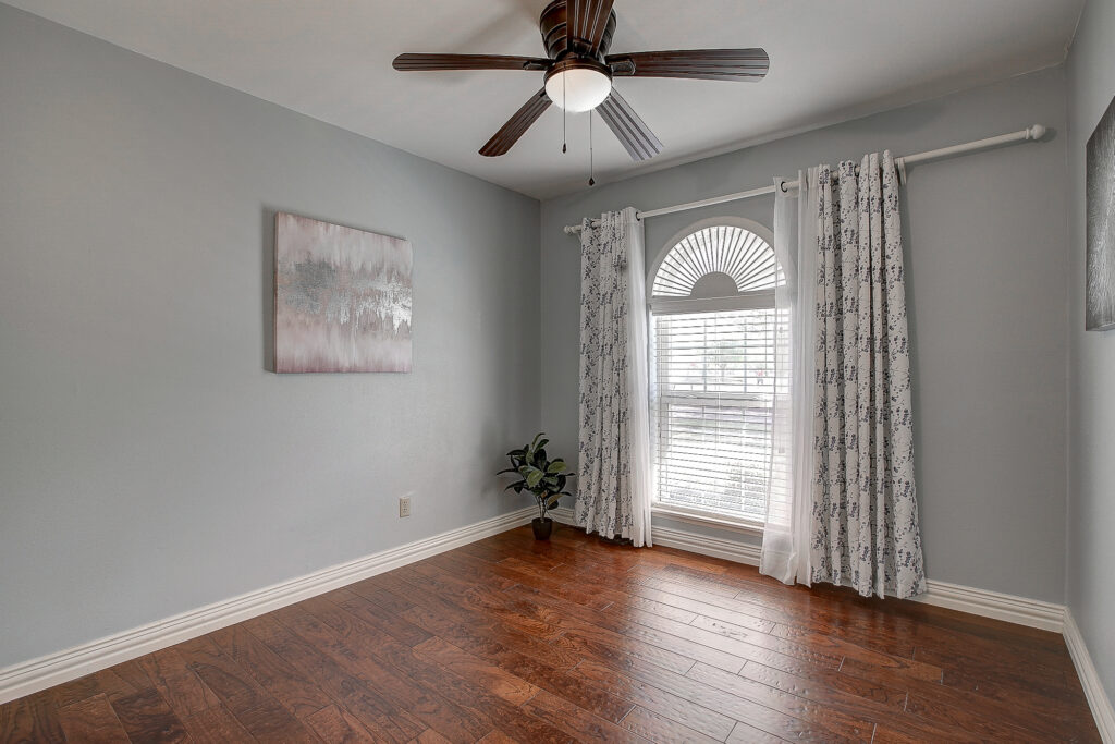 Secondary bedroom at 5302 Saddleback Rd Garland TX with wood flooring, ceiling fan, and arched window with natural light