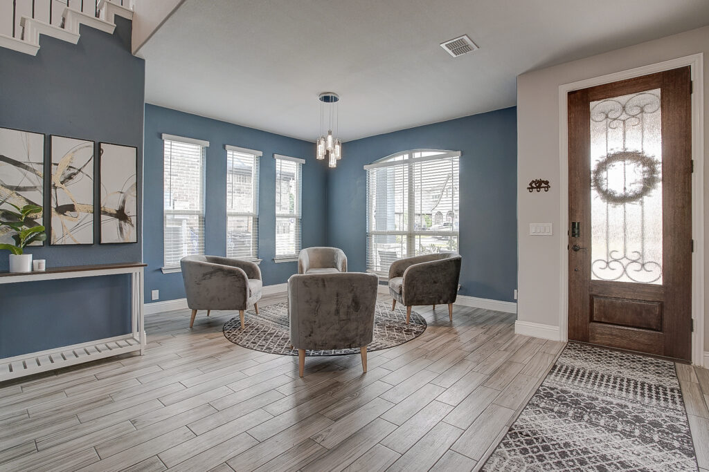 Formal sitting area with tall ceilings, gray wood-look tile flooring, blue accent wall, and natural light in a Lavon TX home