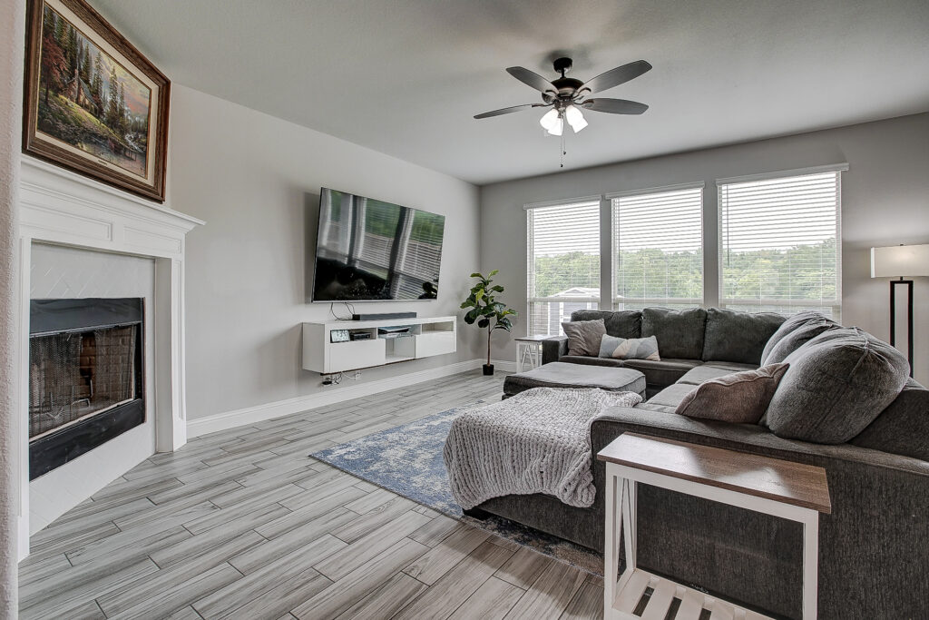 Spacious living room with corner fireplace, large sectional sofa, oversized windows, and backyard views