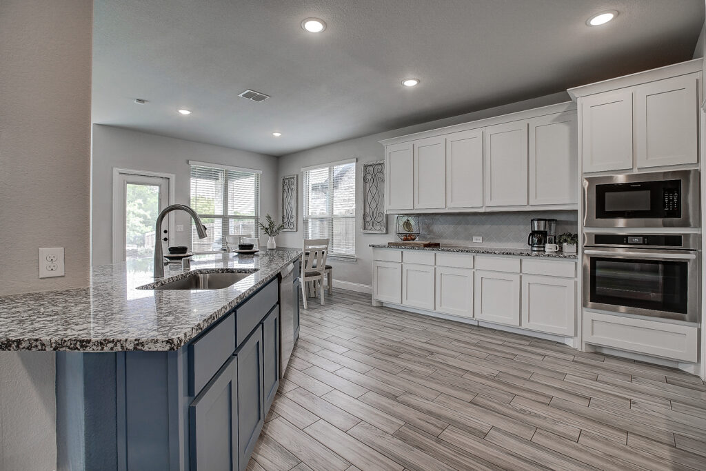 Open kitchen with oversized granite island, white cabinetry, recessed lighting, and stainless appliances
